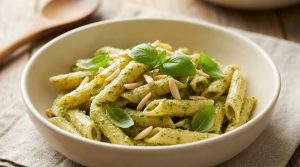 Un bol de penne au pesto d'amande garni de feuilles de basilic frais et d'amandes effilées sur une table en bois.
