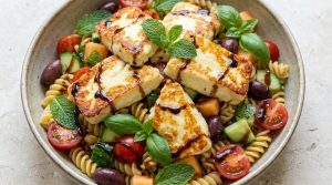 Bol de salade de pâtes fusilli avec du talagani grillé, tomates cerises, olives, concombre et herbes fraîches.