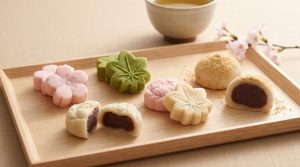 Sélection de wagashi colorés en forme de fleurs et feuilles sur un plateau en bois avec du thé.