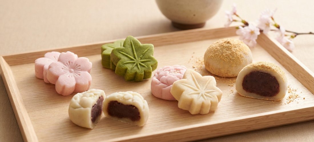 Sélection de wagashi colorés en forme de fleurs et feuilles sur un plateau en bois avec du thé.