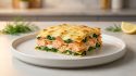 Une part de lasagnes au saumon et aux épinards avec une couche de fromage doré sur une assiette blanche.