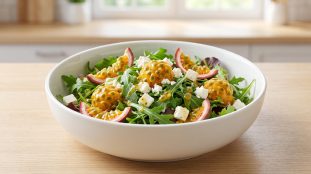 Un bol de salade fraîche composée de roquette, dés de fromage blanc et morceaux de fruit de la passion frais.
