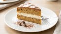 Part de gâteau café chocolat sur assiette blanche, avec glaçage marron et crème blanche. Grains de café et cacao en poudre. Fourchette.